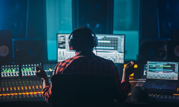 Artist, Musician, Audio Engineer, Producer in Music Record Studi Artist, Musician, Audio Engineer, Producer in Music Record Studio, Uses Control Desk with Computer Screen showing Software UI with Song Playing. Success with Raised Hands, Dances. Back View.